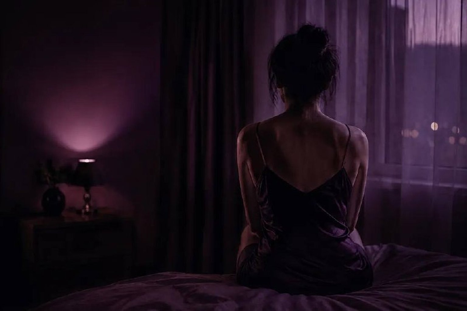Perempuan duduk sendiri di atas katil dalam bilik gelap